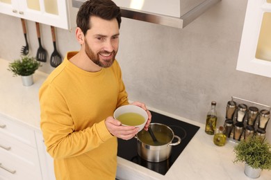 Photo of Man with bowl of delicious soup in kitchen