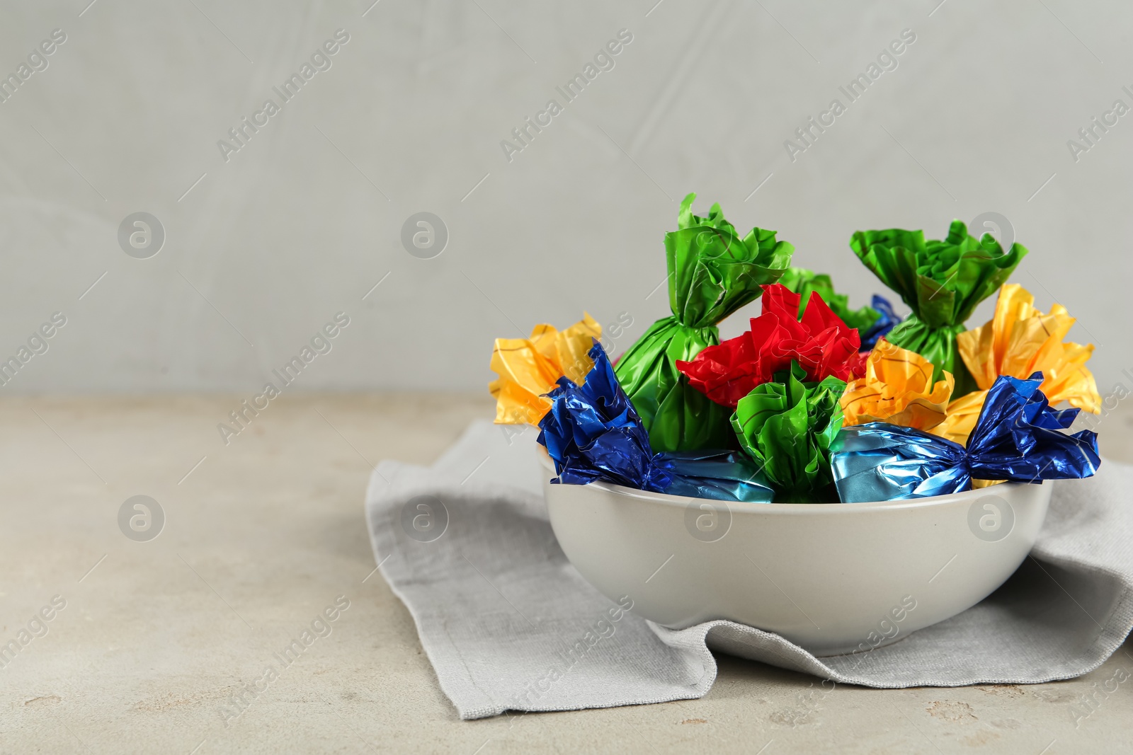 Photo of Candies in colorful wrappers on light beige table, space for text