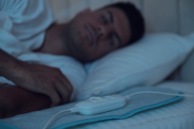 Man sleeping in bed with electric heating pad, focus on cable