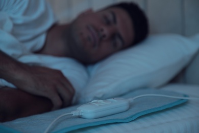 Photo of Man sleeping in bed with electric heating pad, focus on cable