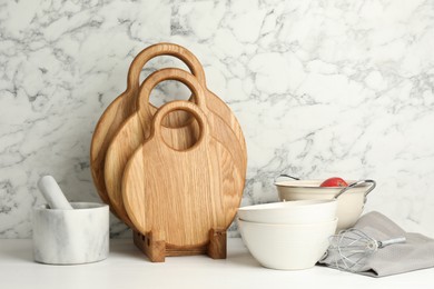 Wooden cutting boards, dishware and kitchen utensils on white table near marble wall