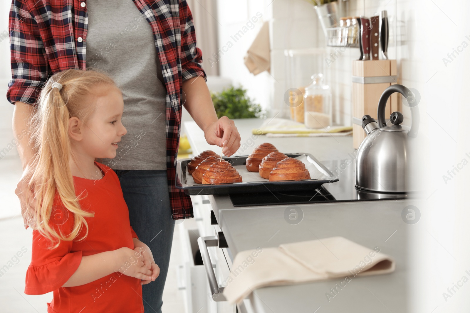 Photo of Daughter and mother with tray of oven baked buns in kitchen