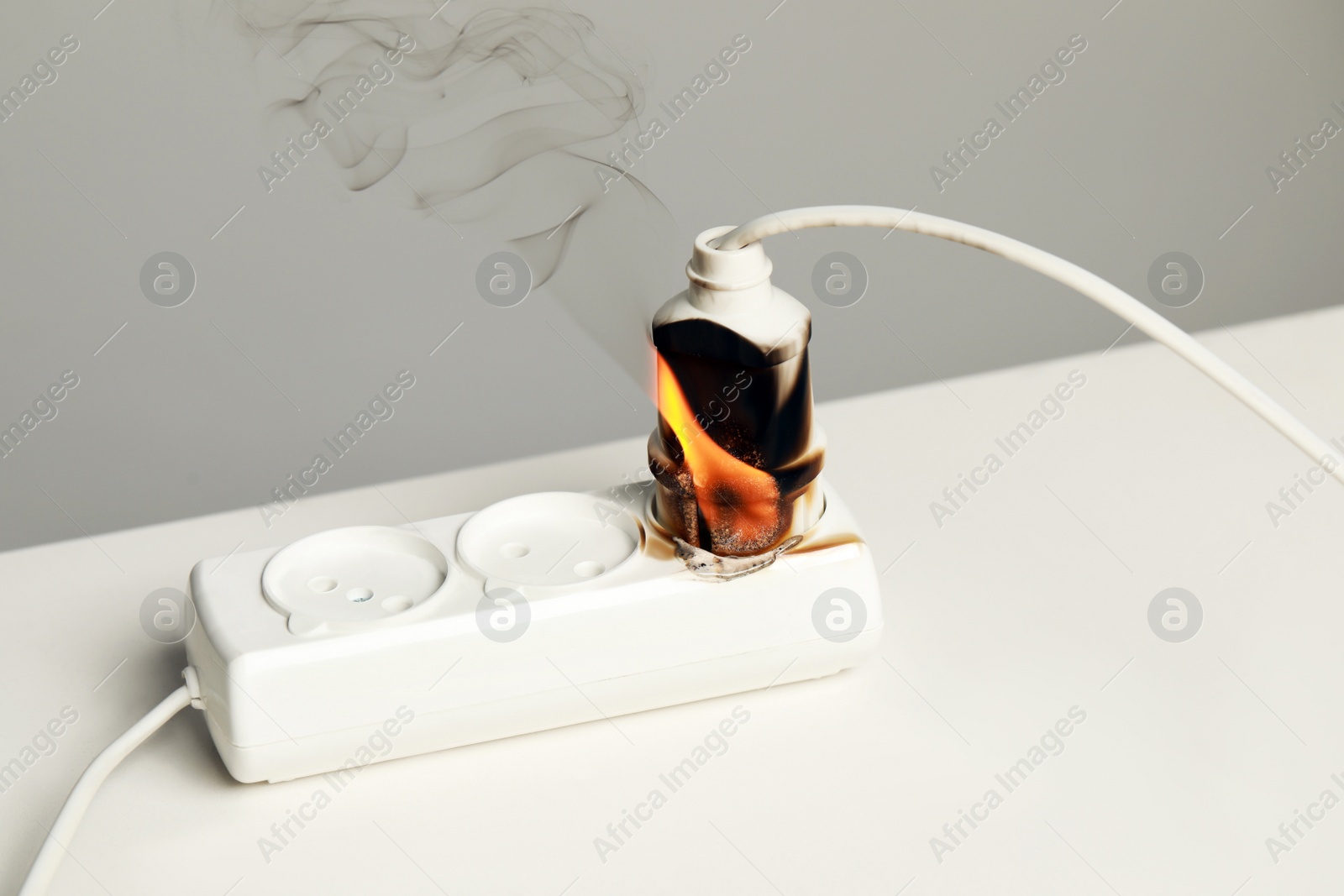 Photo of Inflamed plug in power strip on white table. Electrical short circuit