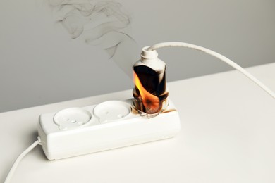 Photo of Inflamed plug in power strip on white table. Electrical short circuit