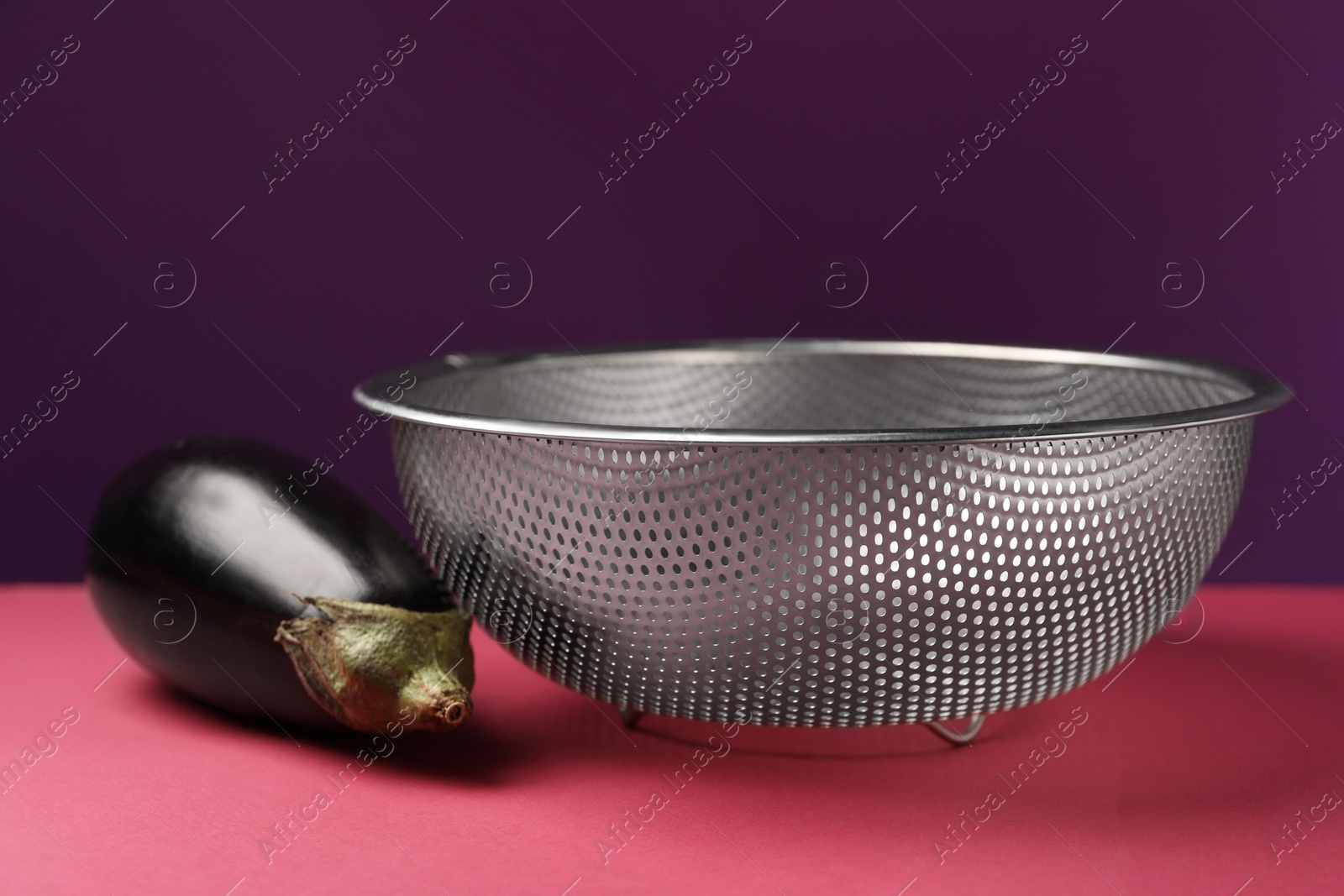 Photo of Colander with fresh eggplant on color background, closeup