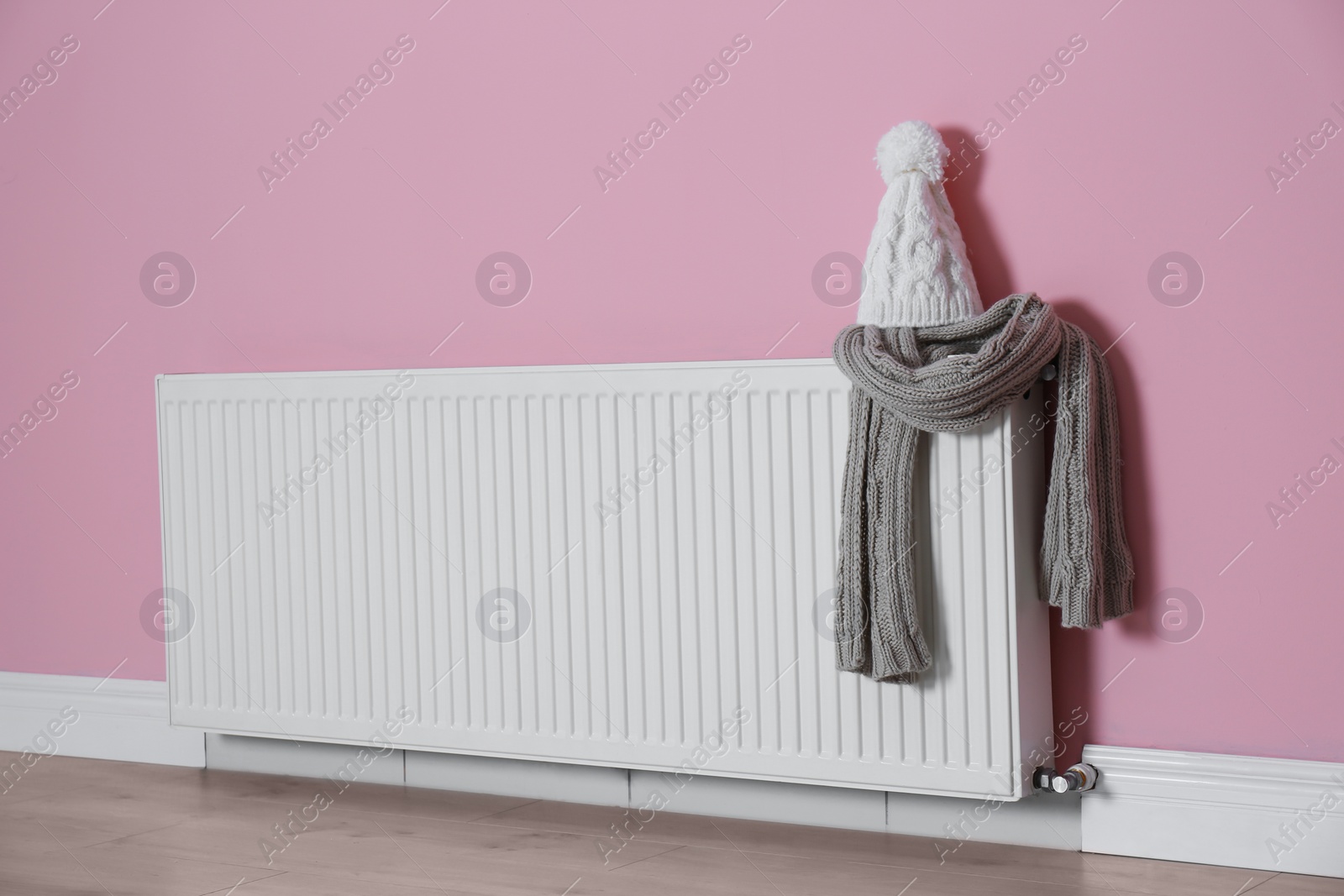 Photo of Modern radiator with knitted hat and scarf near color wall indoors. Central heating system