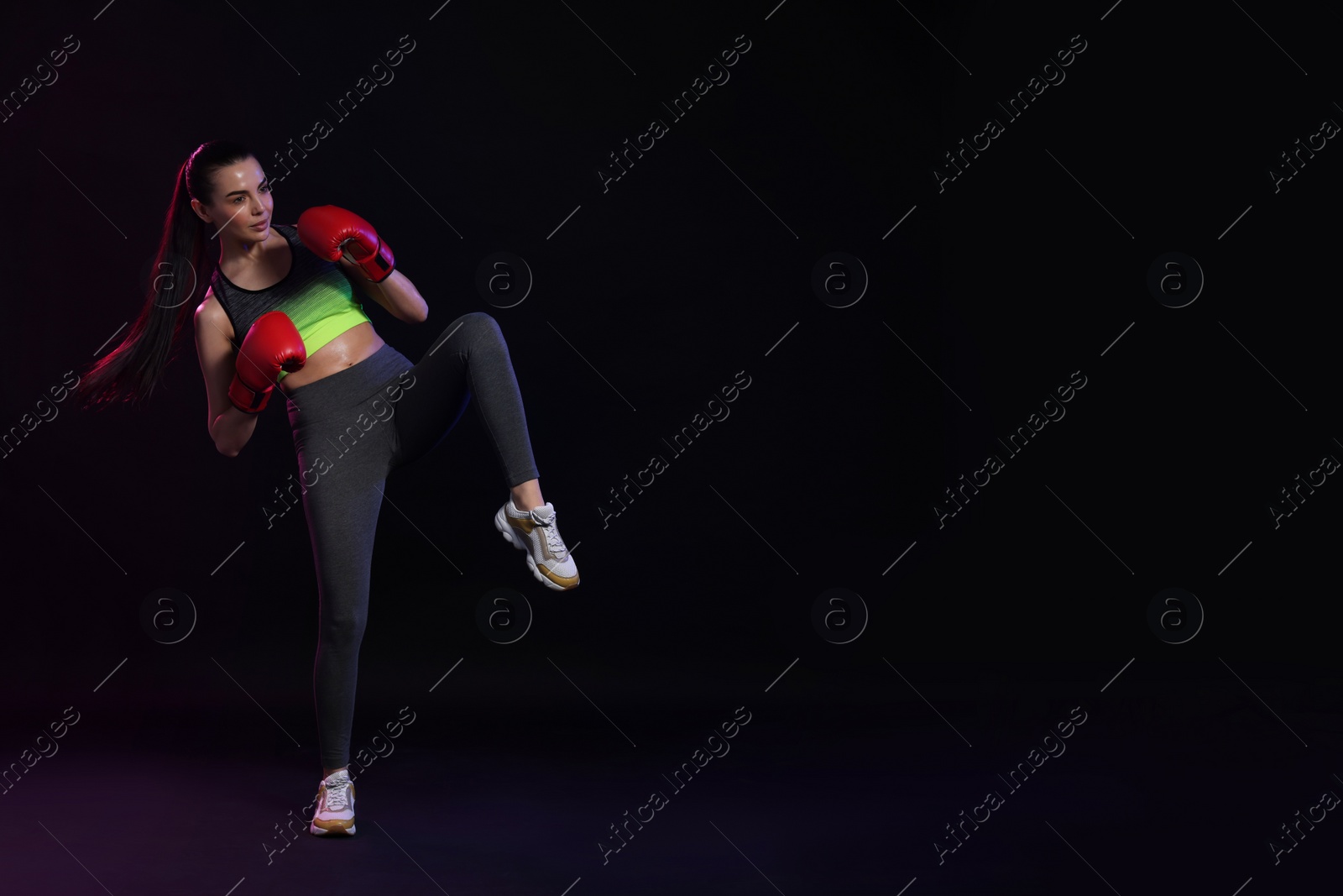 Photo of Beautiful woman in boxing gloves training on black background. Space for text