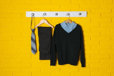 Photo of Shirt, jumper, pants and tie hanging on yellow brick wall. School uniform