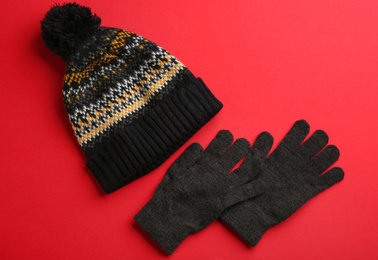 Woolen gloves and hat on red background, flat lay