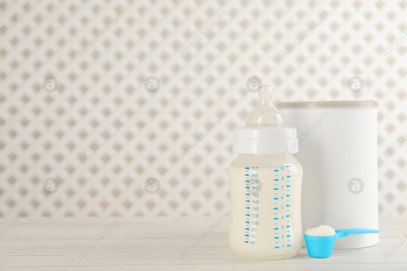 Photo of Blank can of powdered infant formula with feeding bottle and scoop on white wooden table, space for text. Baby milk