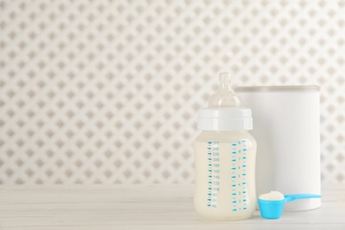 Blank can of powdered infant formula with feeding bottle and scoop on white wooden table, space for text. Baby milk