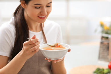 Young woman eating tasty vegetable soup indoors