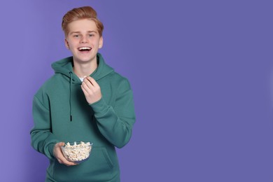 Teenage boy with delicious popcorn on purple background. Space for text