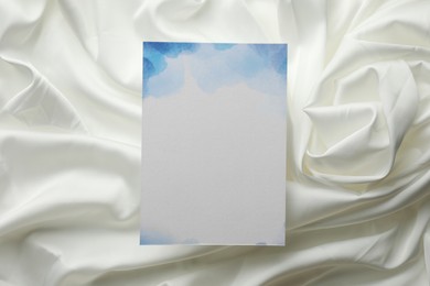 Blank invitation card on white fabric, top view