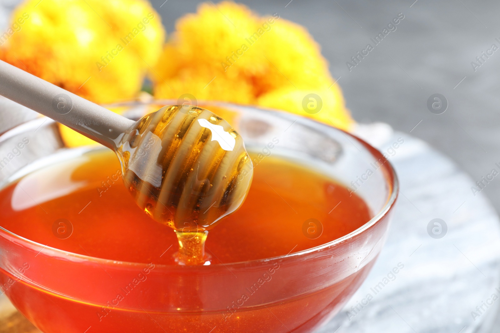 Photo of Glass bowl with organic honey and dipper on board, closeup
