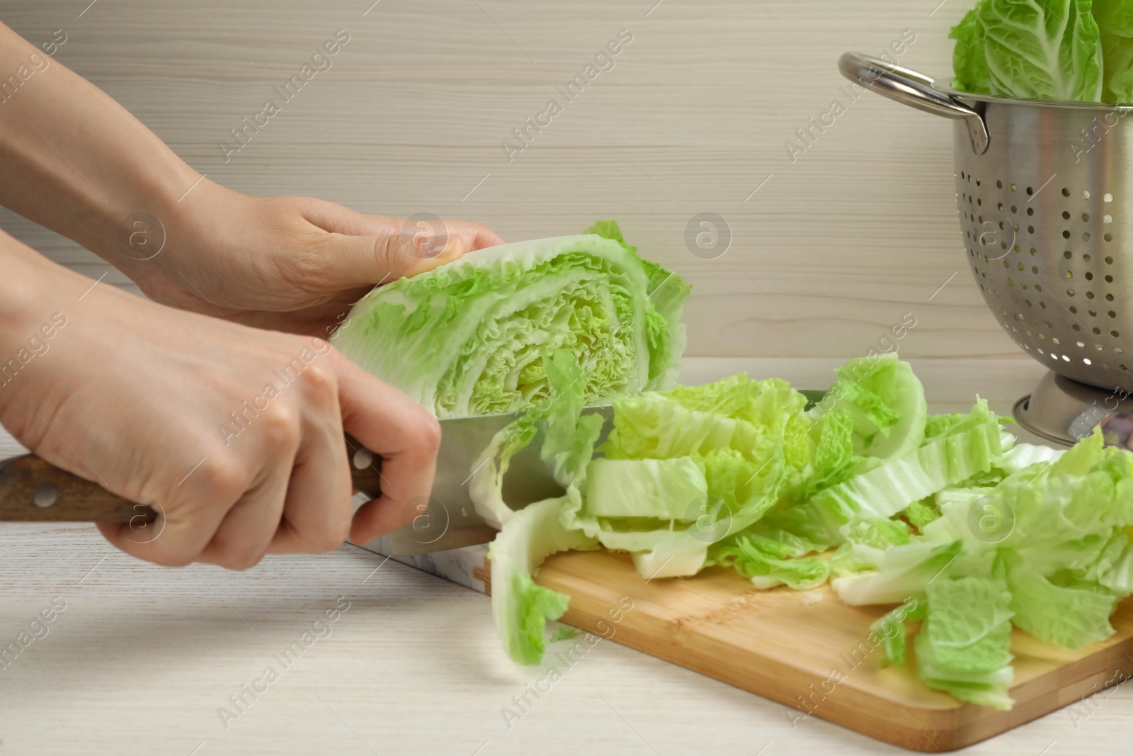 Photo of Woman cutting Chinese cabbage at white wooden kitchen table, closeup