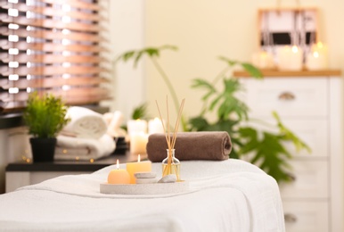 Photo of Composition with reed air freshener, candles and stones on massage table in spa salon. Space for text