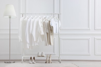 Photo of Rack with different stylish women`s clothes, shoes and lamp near white wall indoors, space for text