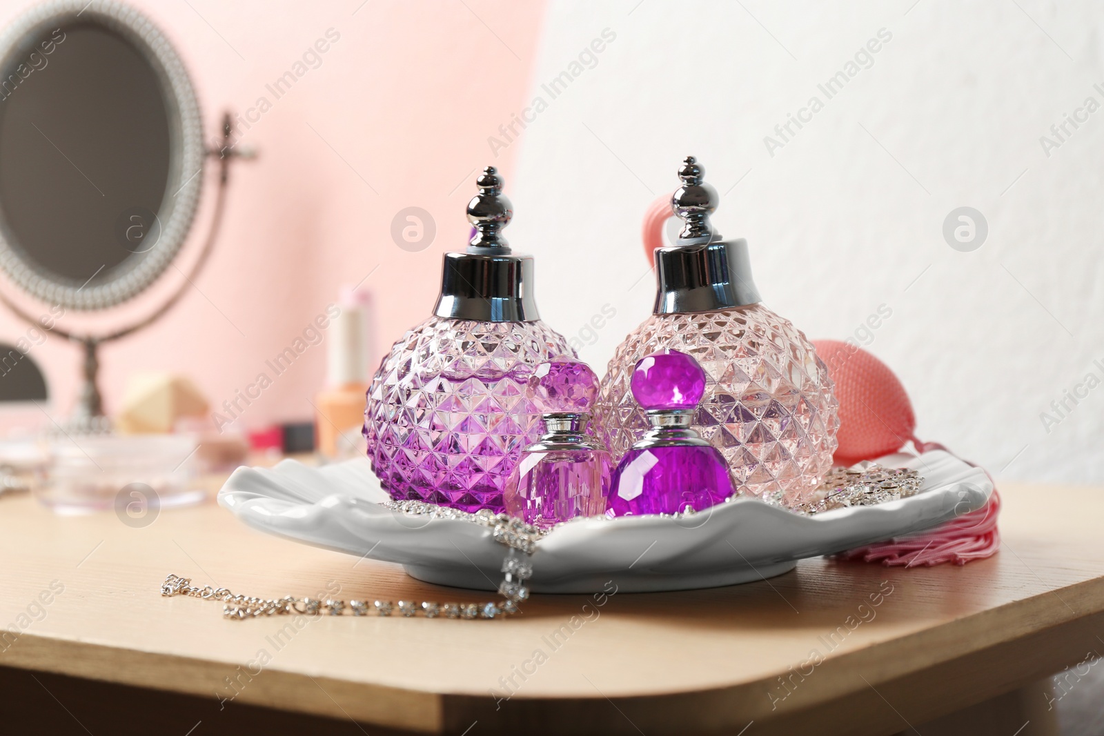 Photo of Plate with perfume bottles and jewellery on dressing table