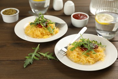 Photo of Tasty spaghetti squash with tomato sauce and arugula served on wooden table