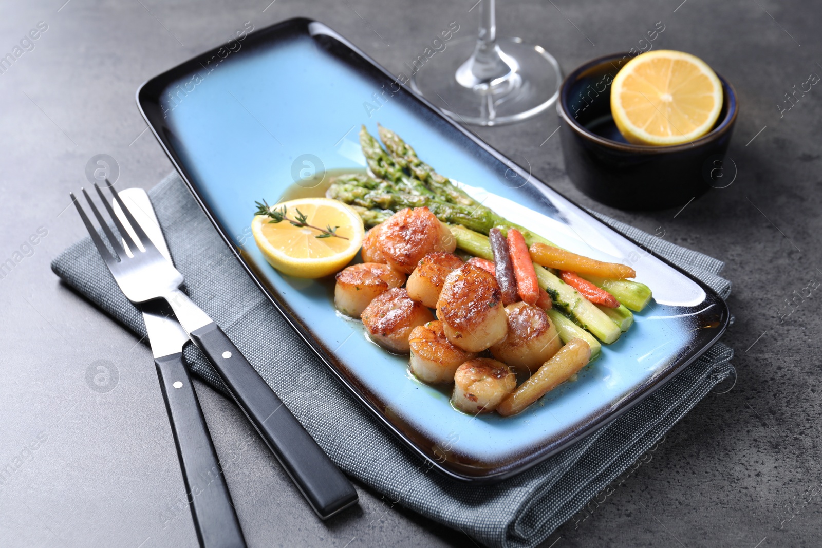 Photo of Delicious fried scallops with asparagus served on grey table