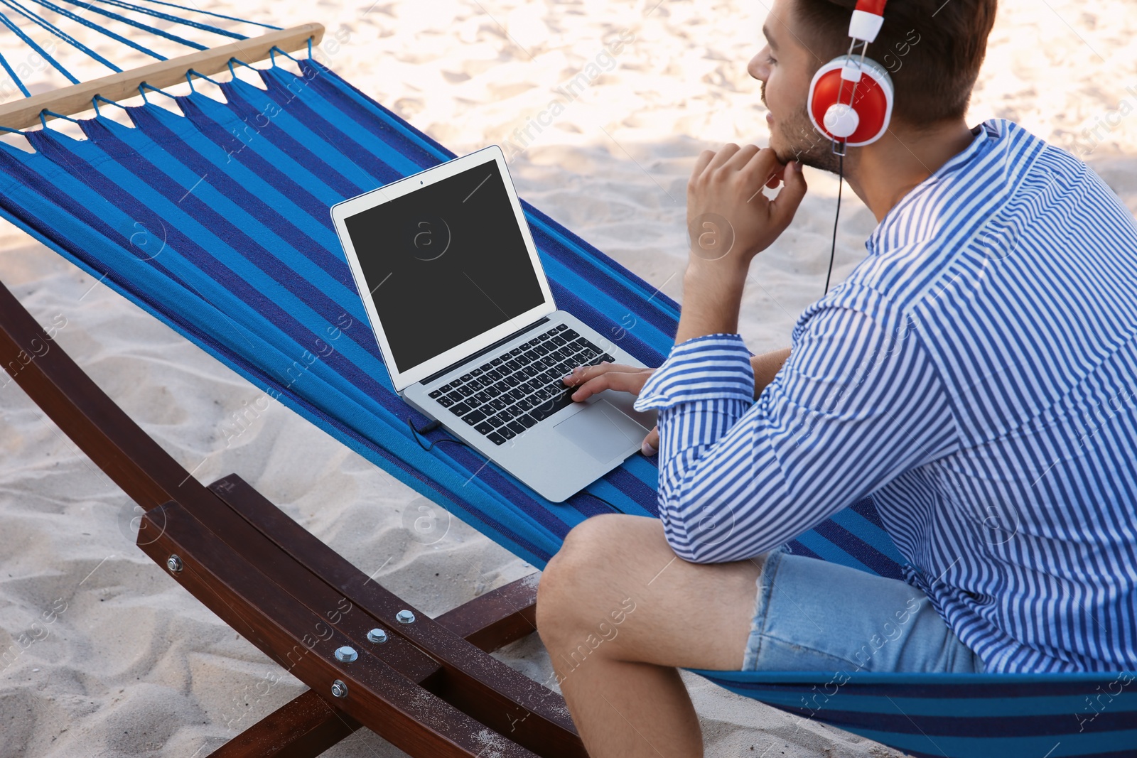 Photo of Young man listening to music in comfortable hammock at seaside