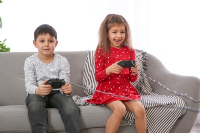 Photo of Cute children playing video game on sofa in living room