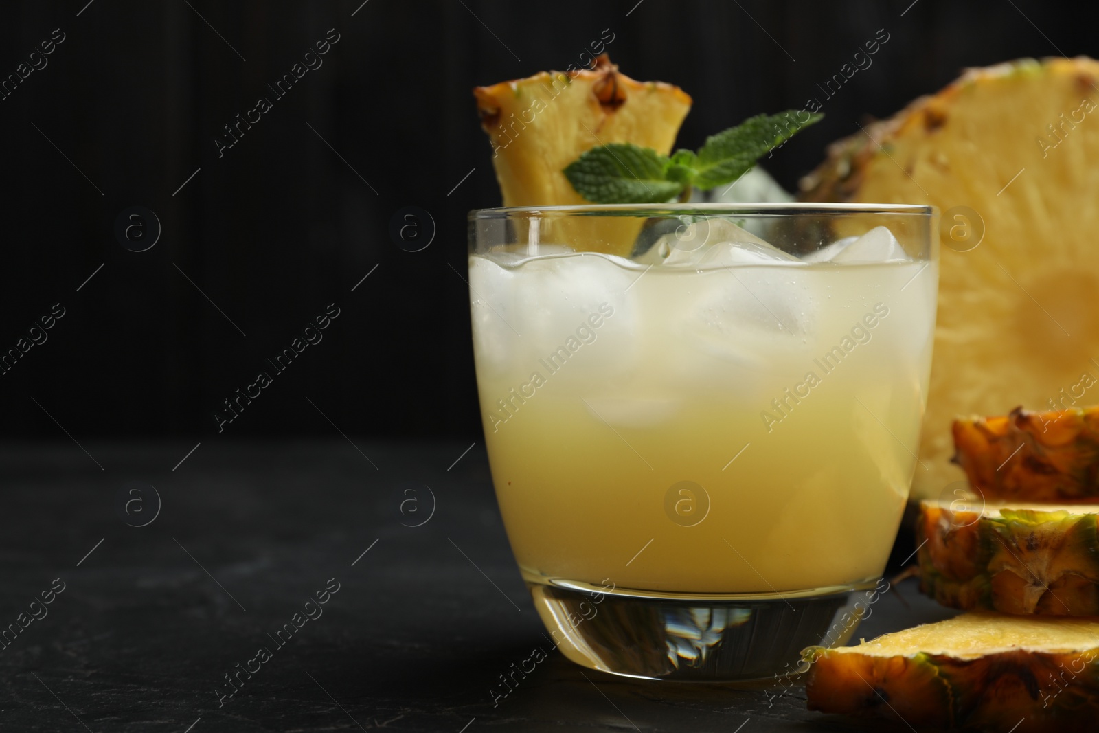 Photo of Delicious pineapple juice with mint and ice cubes on black table, closeup. Space for text