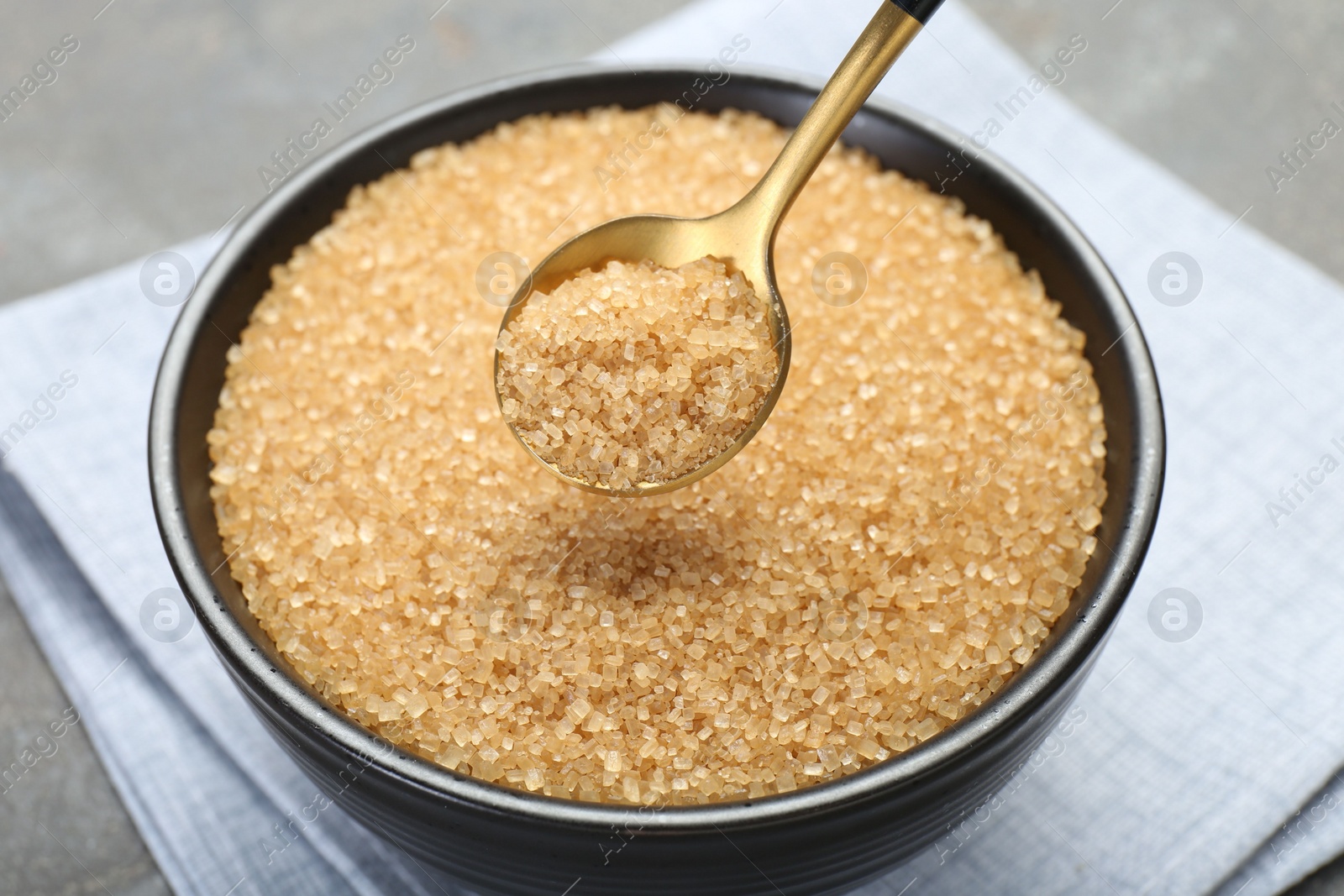 Photo of Taking brown sugar with spoon from bowl at grey table, closeup