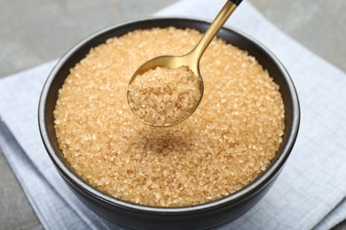 Taking brown sugar with spoon from bowl at grey table, closeup