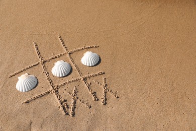 Photo of Playing Tic tac toe game with shells on sand, above view. Space for text