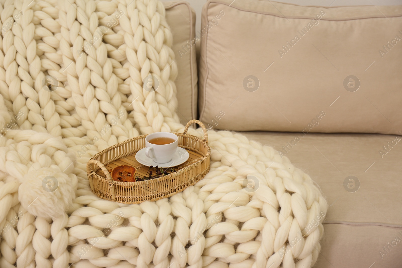 Photo of Tray with cup of tea on white knitted blanket. Interior element