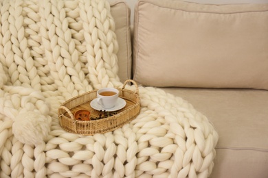 Tray with cup of tea on white knitted blanket. Interior element