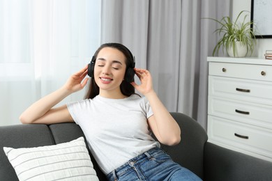 Photo of Happy woman in headphones enjoying music on soft sofa at home