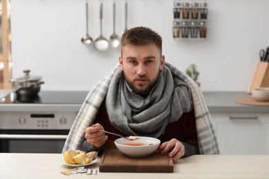 Photo of Sick young man eating tasty soup to cure flu at table in kitchen