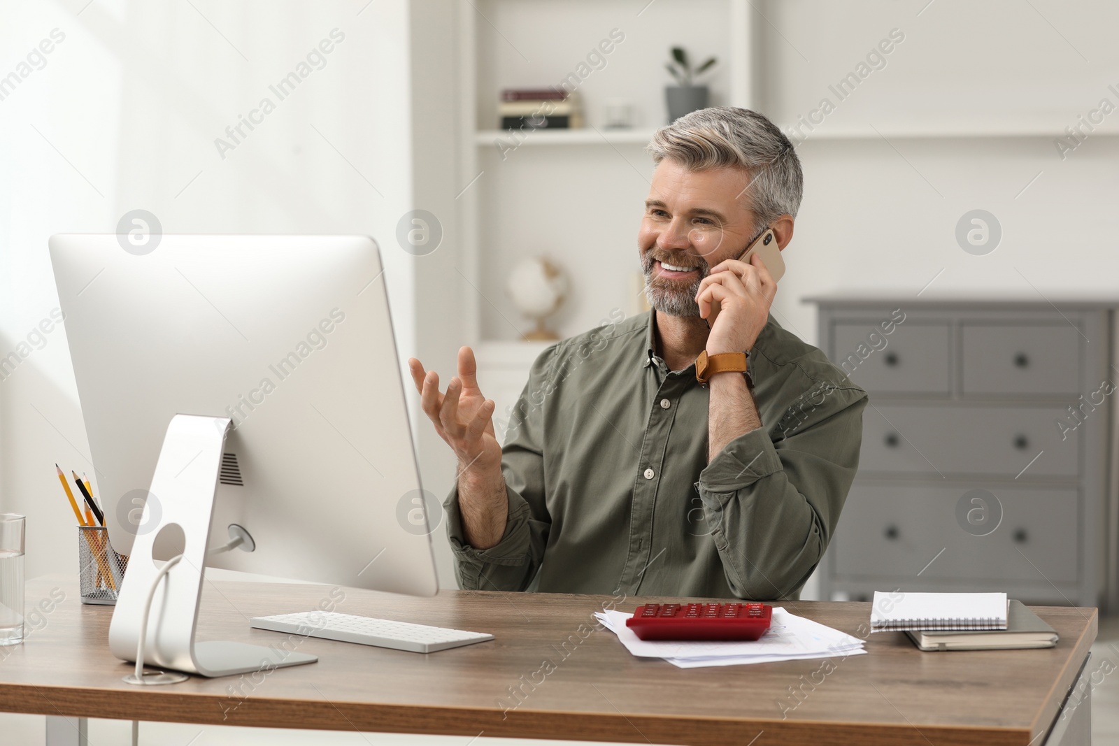 Photo of Professional accountant talking on phone and working at wooden desk in office