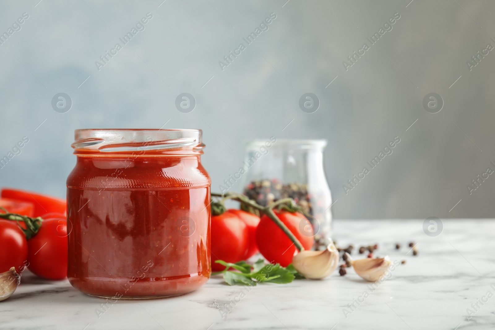 Photo of Composition with jar of tasty tomato sauce on table against grey background. Space for text