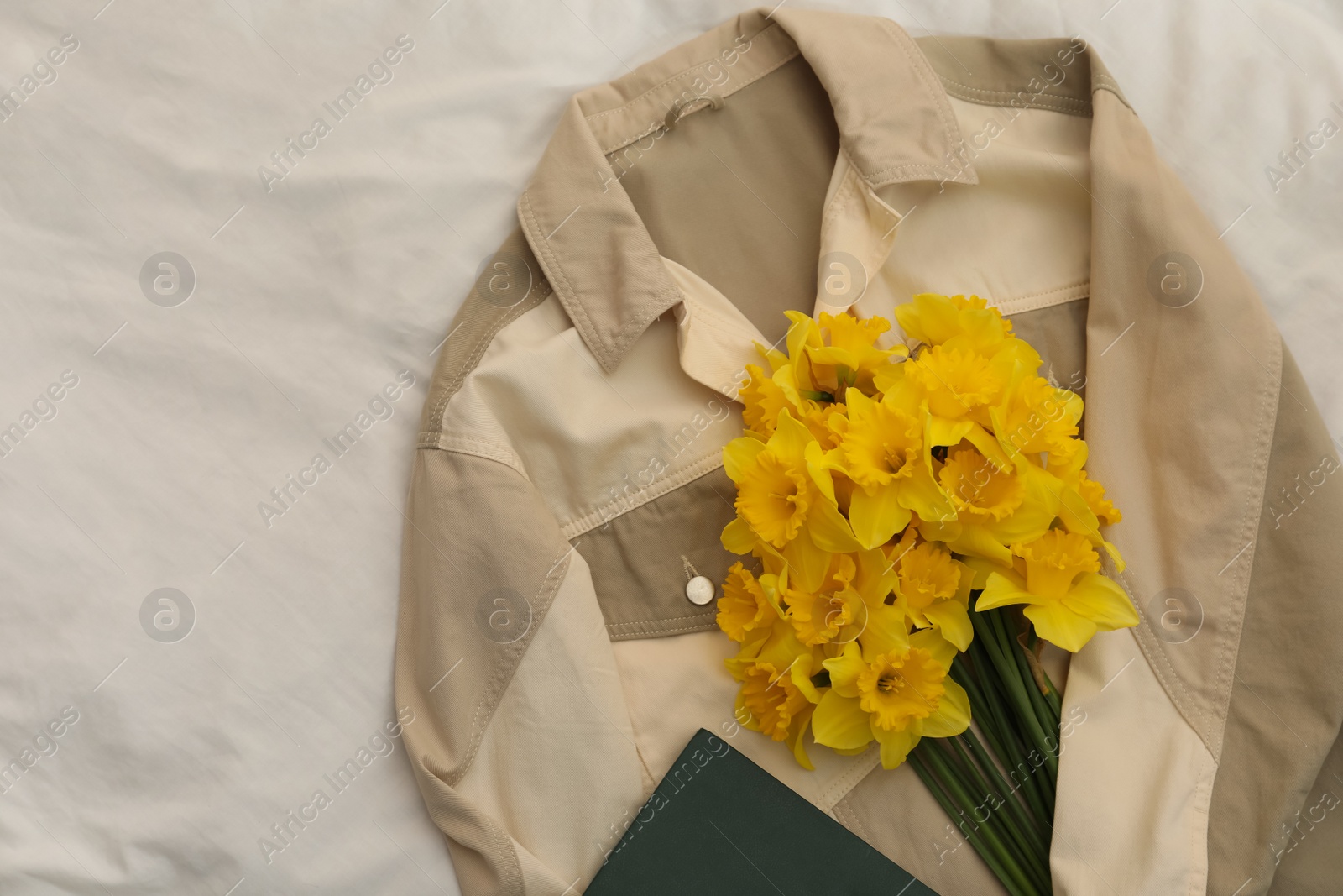 Photo of Beautiful daffodils, shirt and book on bed, flat lay. Space for text