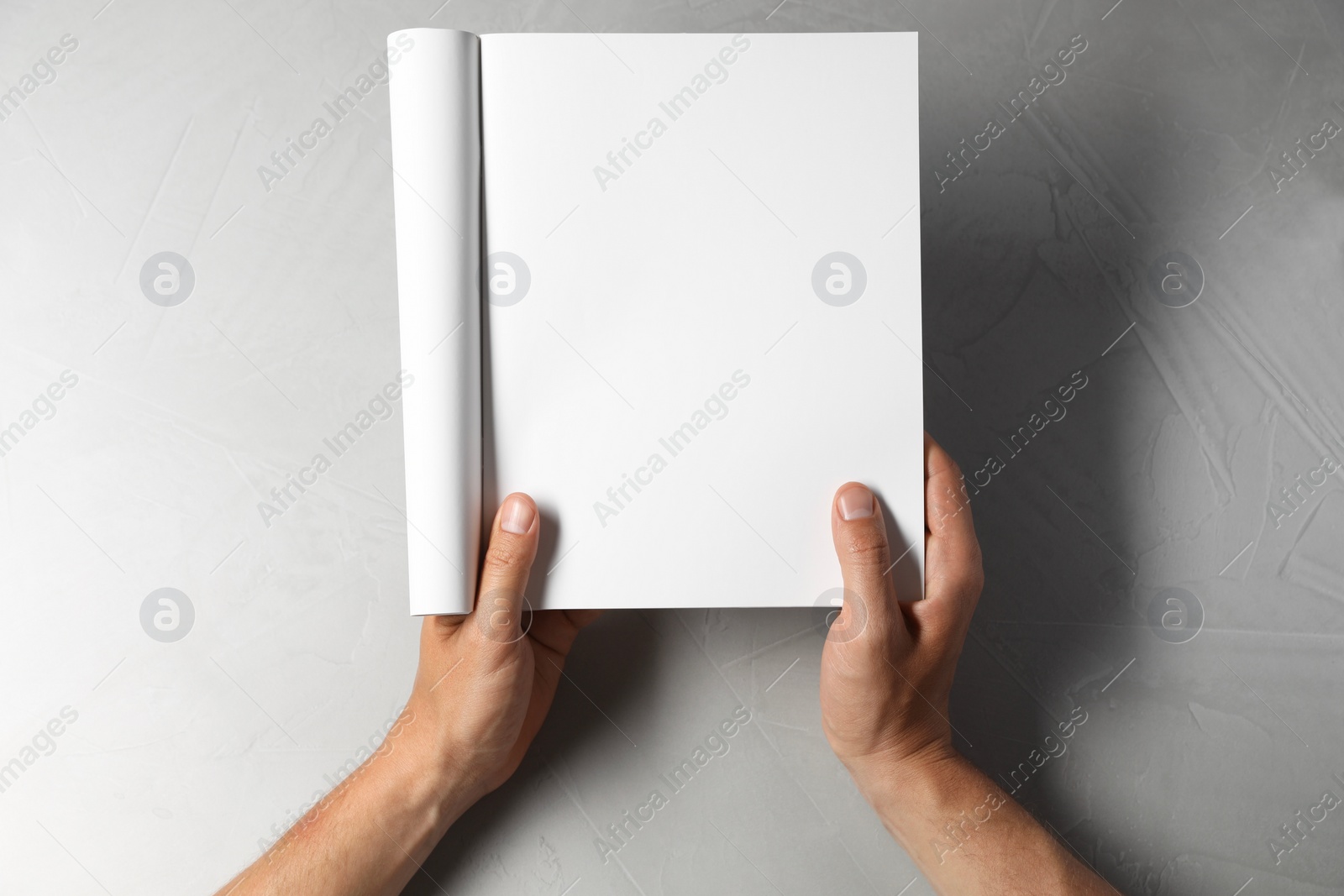 Photo of Man holding blank notebook at light grey table, top view. Mockup for design