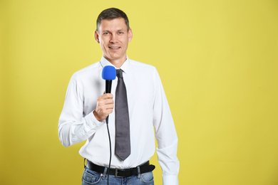 Male journalist with microphone on yellow background