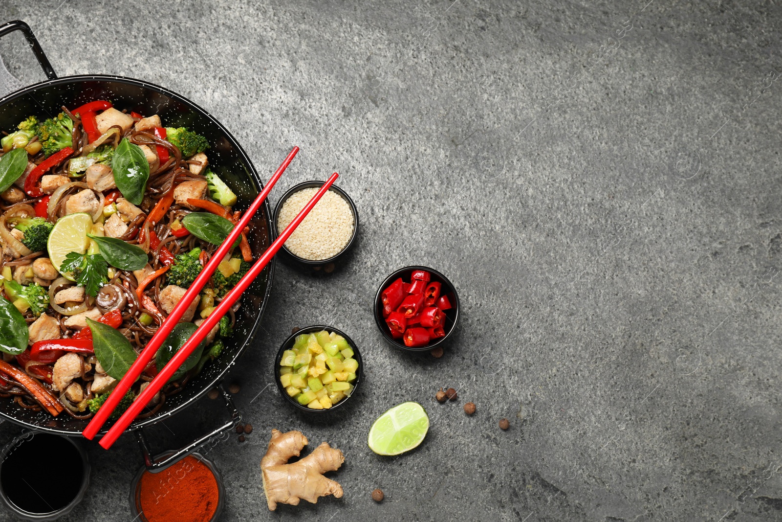 Photo of Stir-fry. Tasty noodles with meat in wok, chopsticks and ingredients on grey textured table, flat lay. Space for text