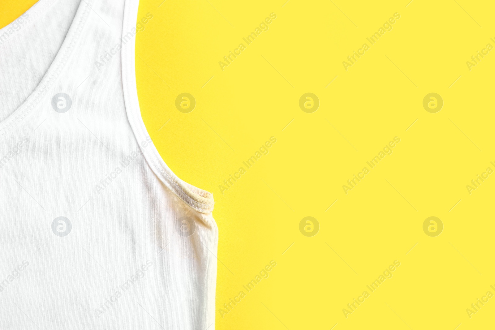 Photo of Undershirt with deodorant stain on yellow background, top view. Space for text