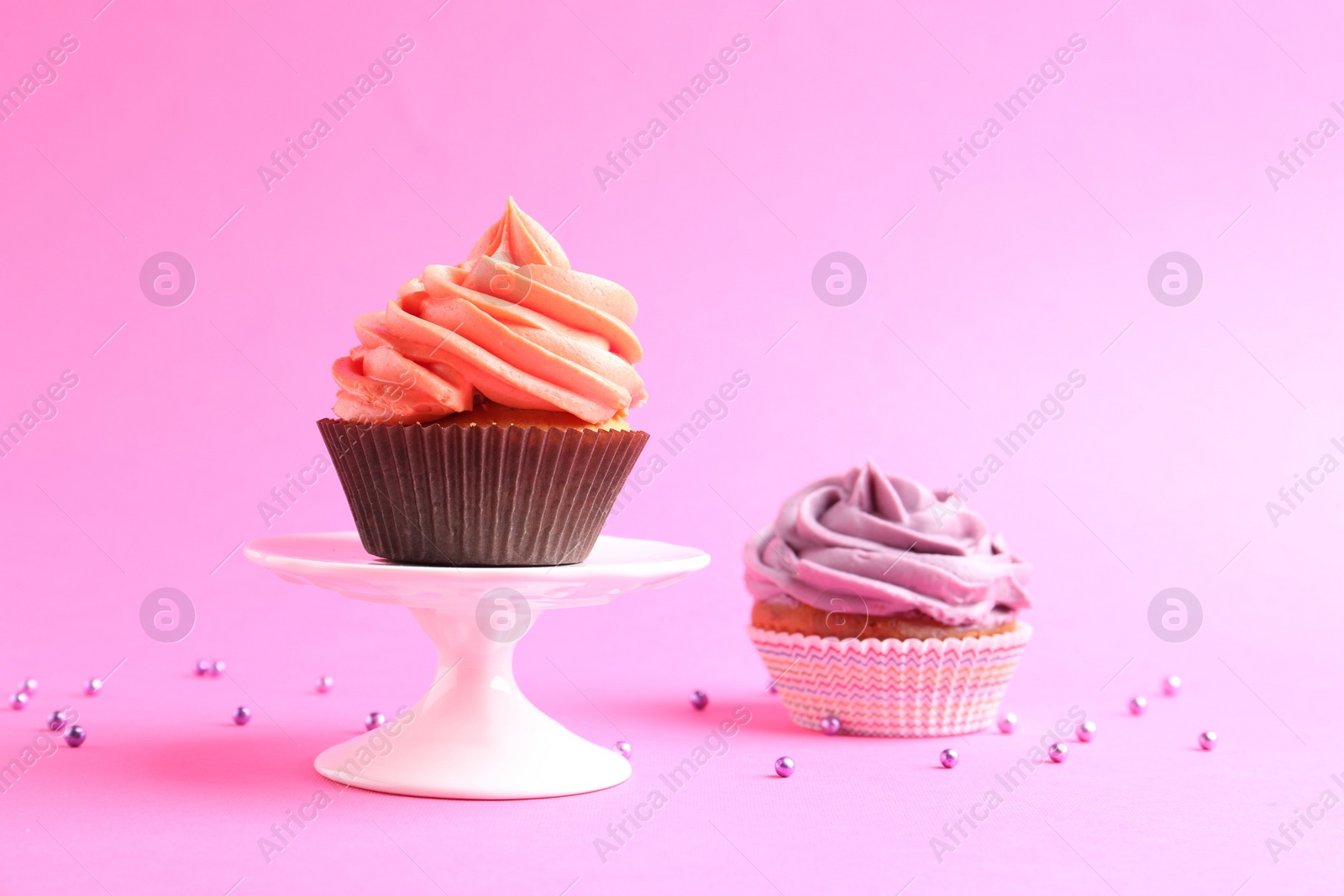 Photo of Delicious cupcakes with bright cream and sprinkles on pink background. Space for text