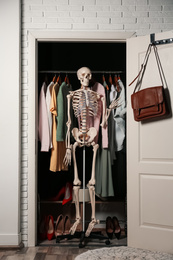 Photo of Artificial human skeleton model among clothes in wardrobe room
