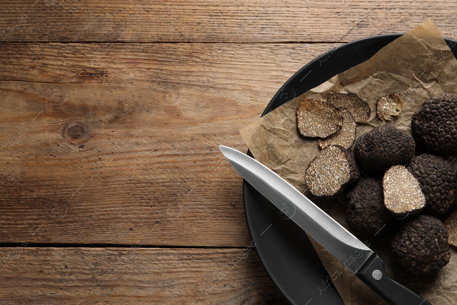 Photo of Black truffles and knife in plate on wooden table, top view. space for text