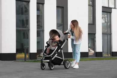Happy nanny with cute little boy in stroller walking outdoors