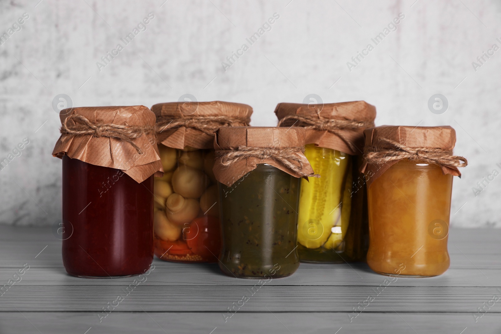 Photo of Many glass jars with different preserved products on wooden table