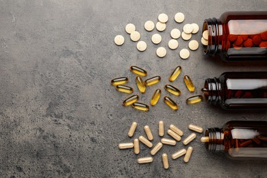 Photo of Overturned bottles with different dietary supplements on grey table, flat lay. Space for text