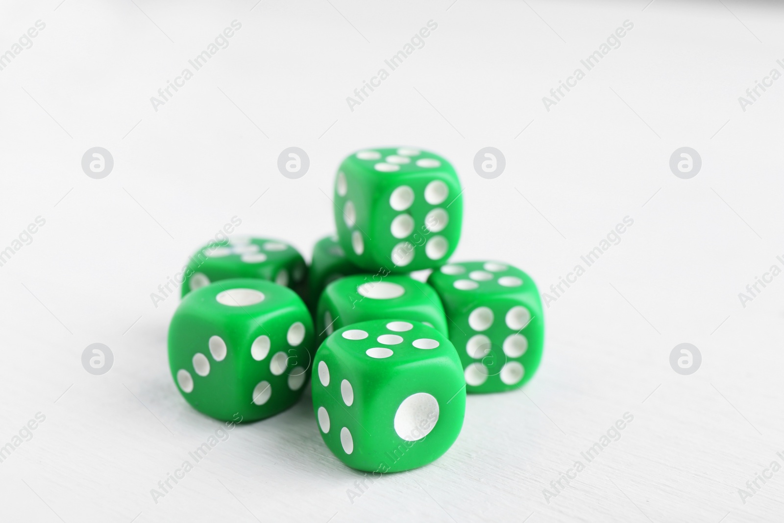 Photo of Many green game dices on white wooden table, closeup