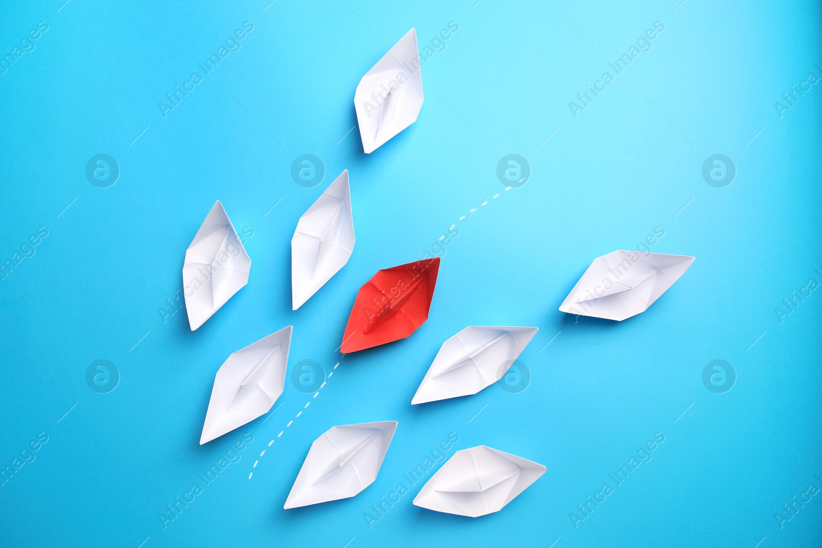 Photo of Red paper boat floating between others on light blue background, flat lay. Uniqueness concept